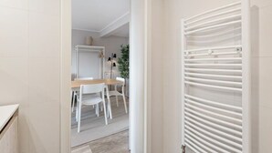 Un baño moderno con azulejos blancos, una bañera blanca y un perchero blanco.