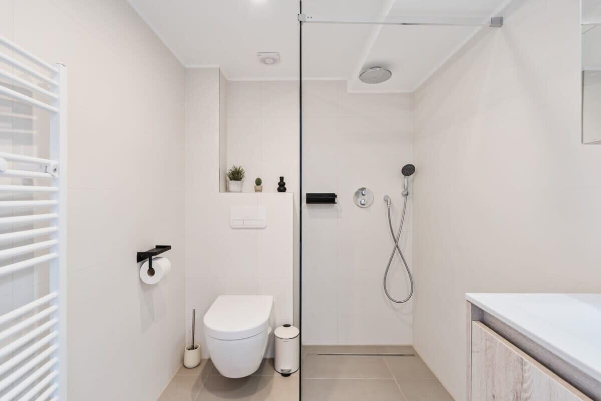 A modern bathroom with a glass shower enclosure, a toilet, a bidet, and a sink with a white countertop.