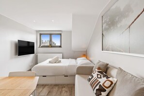 A modern, well-lit room with a bed, a sofa, a TV, and a window with a view of buildings. - Modern Studio in Limpertsberg Near City Center (Luxembourg)