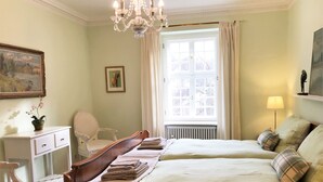 A bedroom with two beds, a white dresser, a chair, a window with curtains, a radiator, and a chandelier. - Apartment in a half-timbered house 4 km to the ski lift carousel or Rothaarsteig (Winterberg)