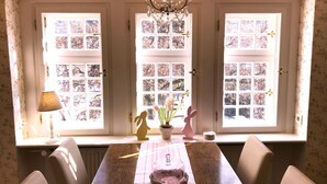 A dining area with a table set for four, a chandelier, and a view through three windows with floral patterns. - Apartment in a half-timbered house 4 km to the ski lift carousel or Rothaarsteig (Winterberg)