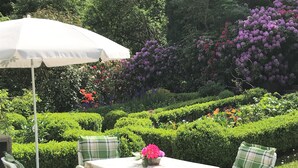 An outdoor seating area with a table and chairs, surrounded by well-manicured hedges and flowering plants. - Apartment in a half-timbered house 4 km to the ski lift carousel or Rothaarsteig (Winterberg)
