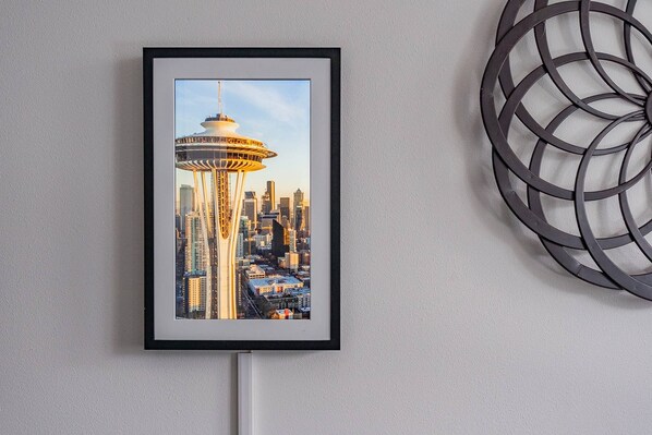 Fotografia emoldurada de um horizonte urbano com uma torre imponente, pendurada em uma parede com um detalhe metálico decorativo à direita.