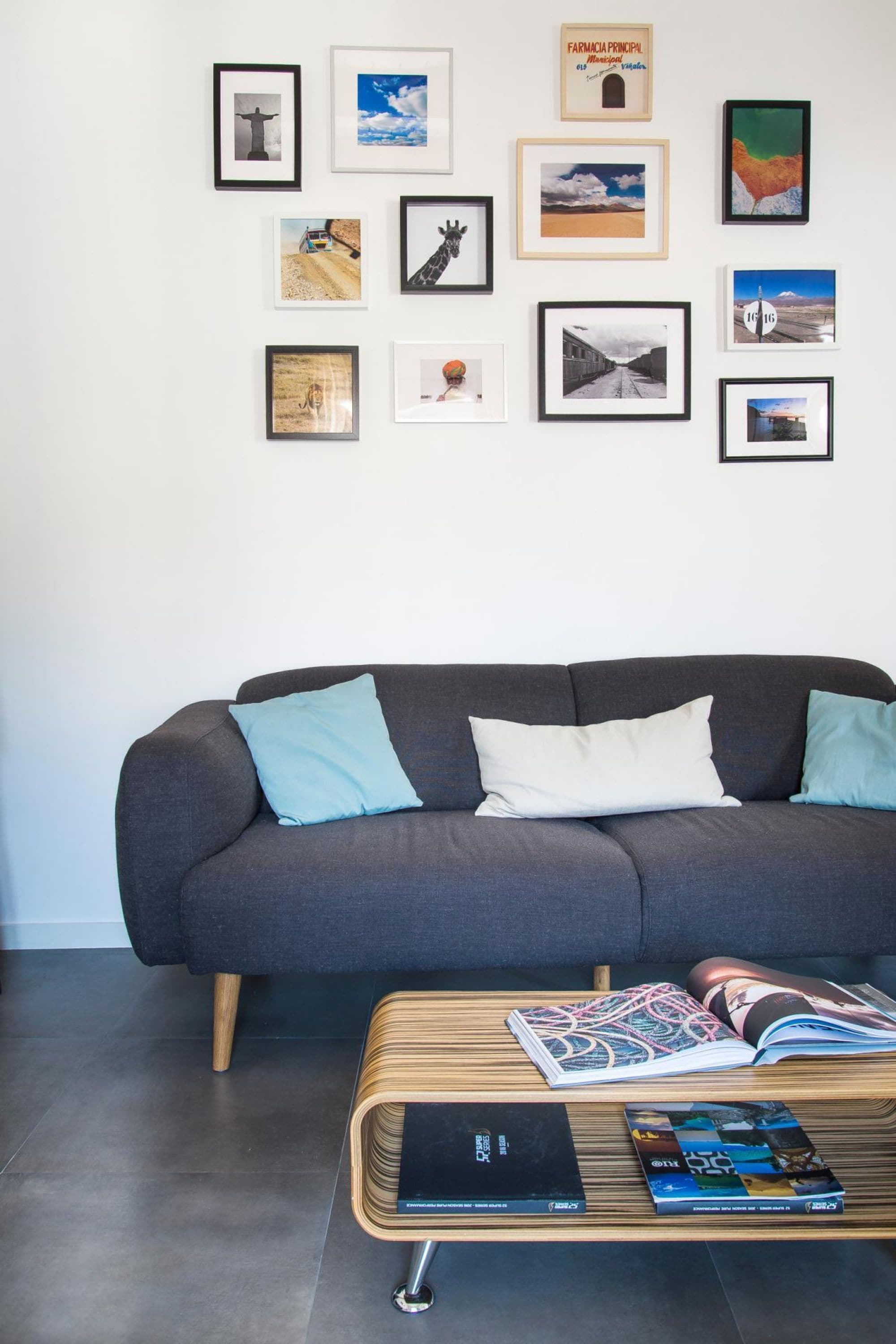 Una sala de estar moderna con un sofá gris oscuro, dos cojines azul claro y una mesa de centro de madera con revistas y un libro.