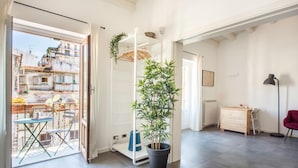 Um quarto claro com varanda, um vaso de planta, uma escrivaninha e uma cadeira.