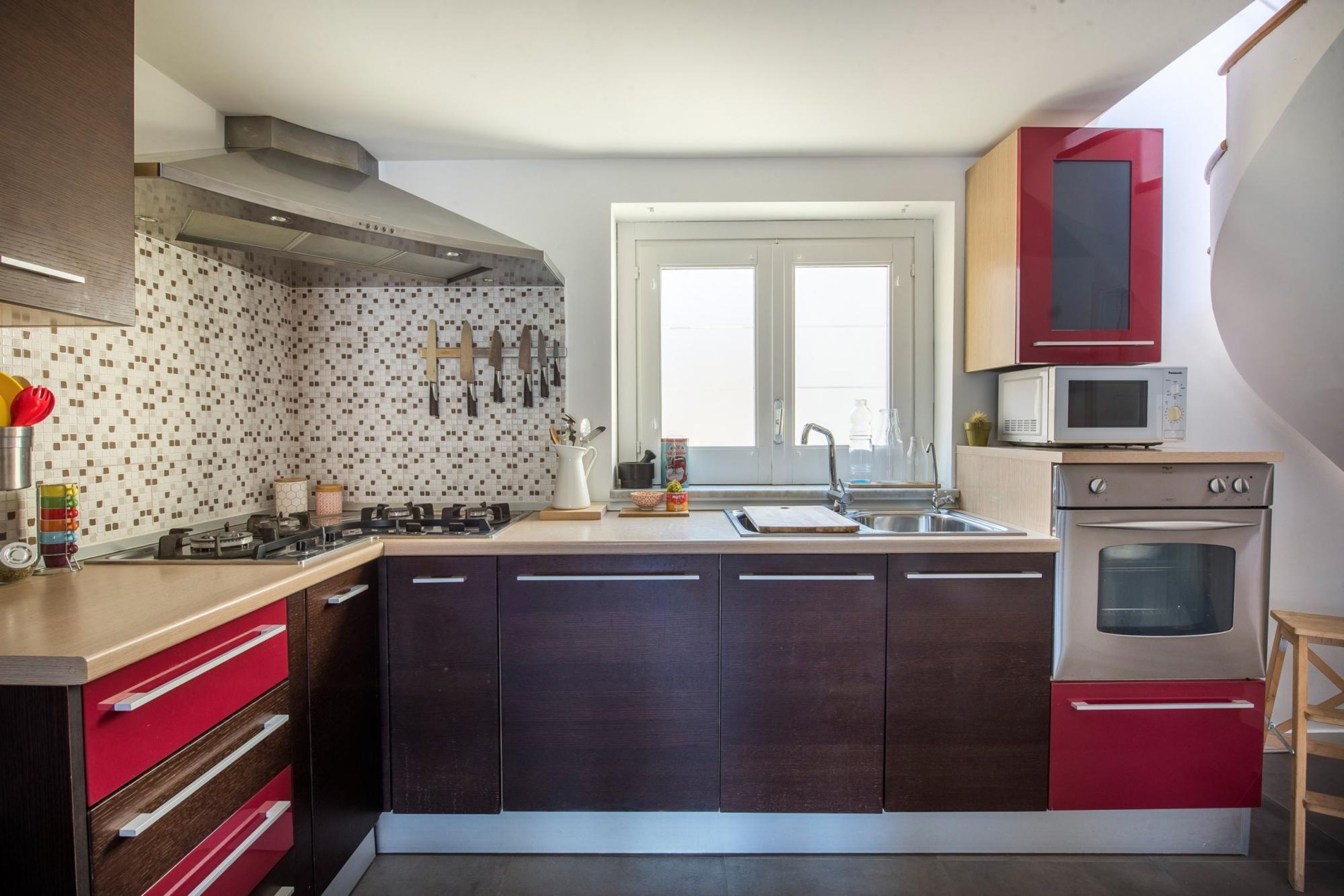 Une cuisine moderne avec des meubles de couleur sombre, un four à micro-ondes, un four traditionnel et une fenêtre au-dessus de l’évier.