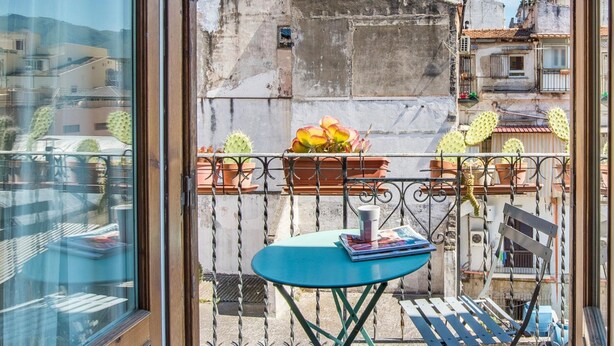 Uma varanda com mesa e cadeiras azuis, plantas em vasos e vista para edifícios.