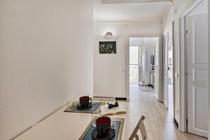 A hallway with a dining table set with a red mug, a glass, and a book. There is a painting on the wall and a door leading to another room. - A Pochi Passi da Piazza de Ferrari (Genoa)