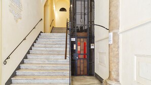 A marble staircase leading to a door with a metal gate, a small sign, and a wall-mounted light fixture. - A Pochi Passi da Piazza de Ferrari (Genoa)