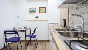 A compact kitchen with a sink, stove, and two chairs. There are two framed pictures on the wall above the counter. - Tribunali Family Apartment by Wonderful Italy (Naples)