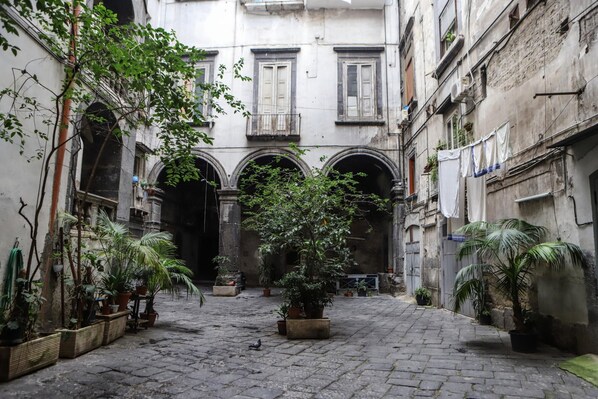 A narrow courtyard with stone paving, surrounded by buildings with arched doorways and balconies.
