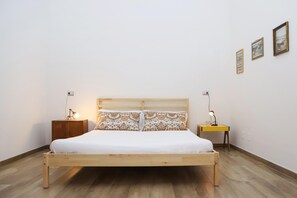 A single-bed room with a wooden headboard, two bedside tables, and a plain white wall with three framed pictures.