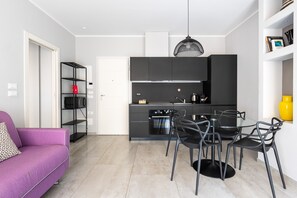 A modern kitchen with black cabinets, a dining area with black chairs, and a purple sofa. - Casa Design di Via Goito by Wonderful Italy (Bologna)