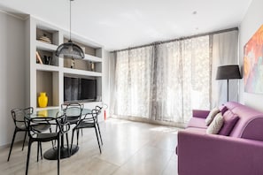 A modern living room with a glass dining table, black chairs, a purple sofa, and a large TV on a white wall. - Casa Design di Via Goito by Wonderful Italy (Bologna)