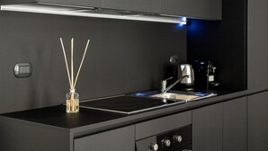 A modern kitchen with dark cabinetry, a stainless steel range hood, a built-in oven, and a coffee maker.