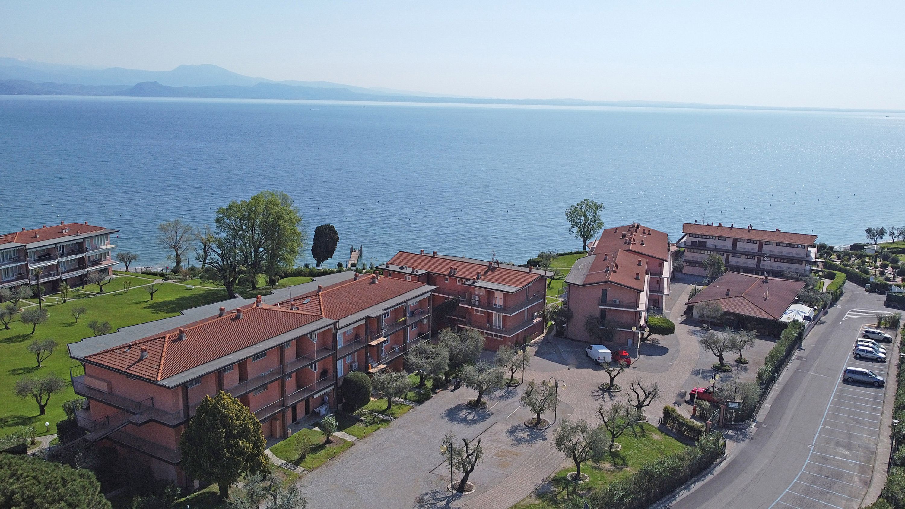 A coastal hotel with multiple buildings, a parking area, and a view of the sea.