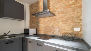 A kitchen with a brick wall, stainless steel cabinets, a microwave, and a modern range hood. - San Michele Apartments - Lapis by Wonderful Italy (Bologna)
