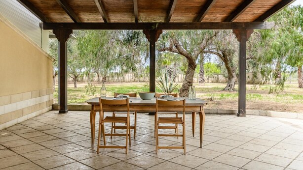 Un patio al aire libre con una mesa y sillas de madera, rodeado de árboles y un suelo de baldosas.