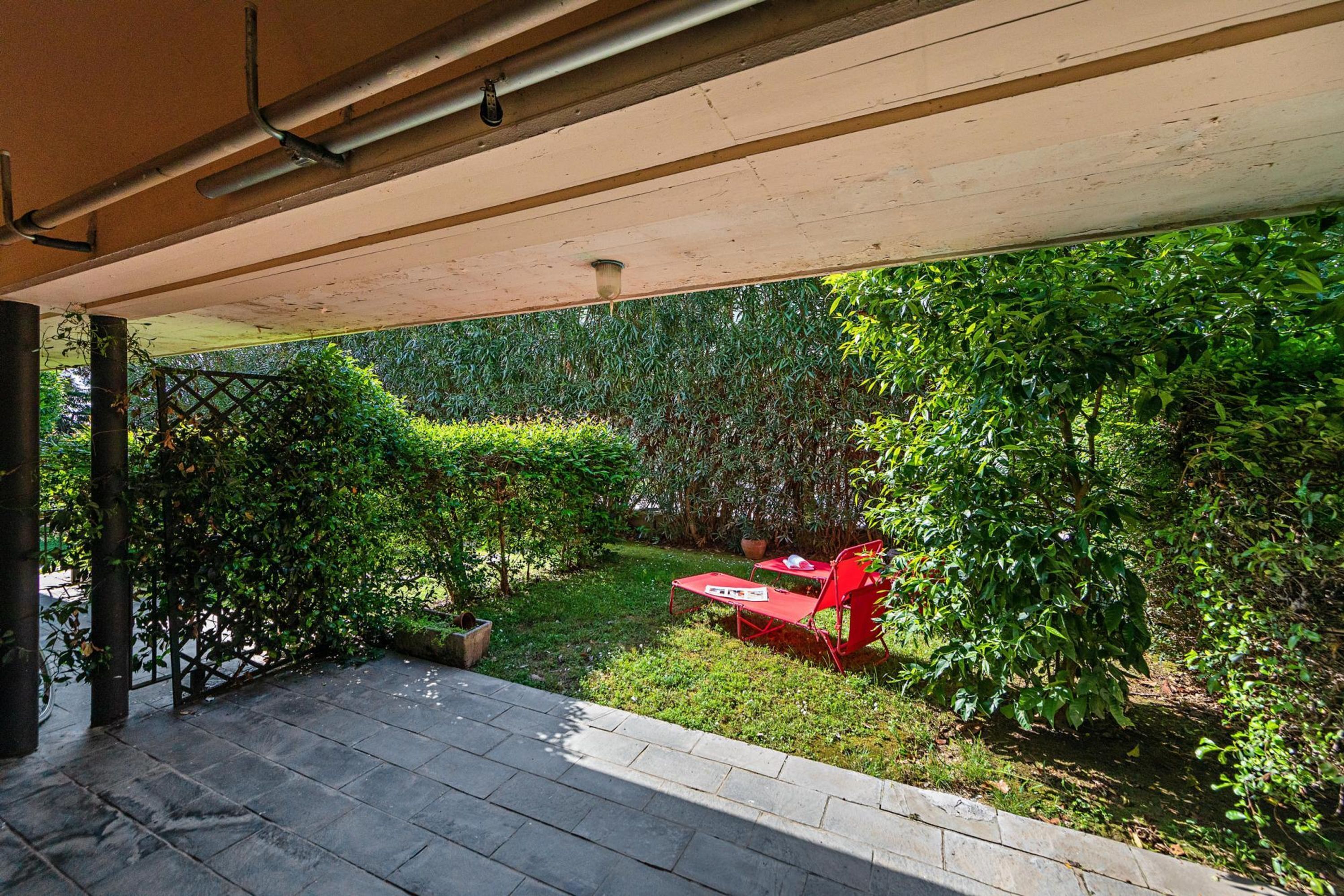 A covered patio area with a seating arrangement and a garden view.