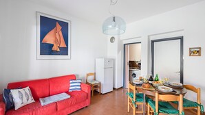 Un espacio habitable pequeño con un sofá rojo, una mesa de comedor preparada para cuatro personas, una zona de cocina y una obra de arte grande enmarcada en la pared.
