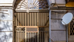 L’entrée d’un immeuble, ornée d’un portail en métal décoratif, d’une antenne parabolique et donnant sur une rue pavée.