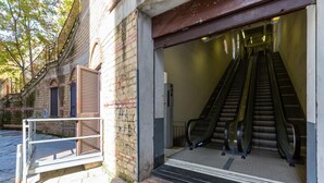 Une entrée avec un escalier et un escalateur, des murs en briques et un portail en métal.