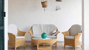 Ein Zimmer mit Korbmöbeln, einer hängenden Pflanzkorb und einer kleinen Schiffverzierung an der Wand.