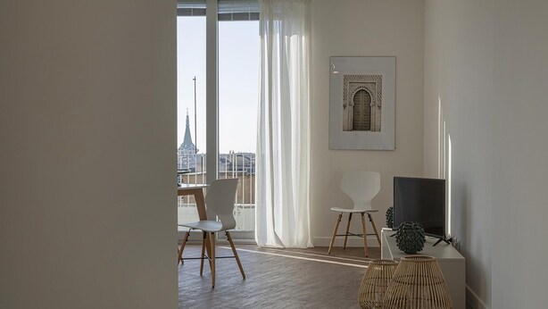 Una sala de estar moderna con un ventanal grande, una zona de comedor con sillas, un televisor de pantalla plana y un adorno de pared decorativo.