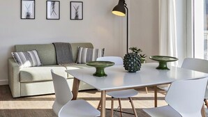 Una sala moderna con un sofá, una mesa de comedor con sillas y obras de arte enmarcadas en la pared.