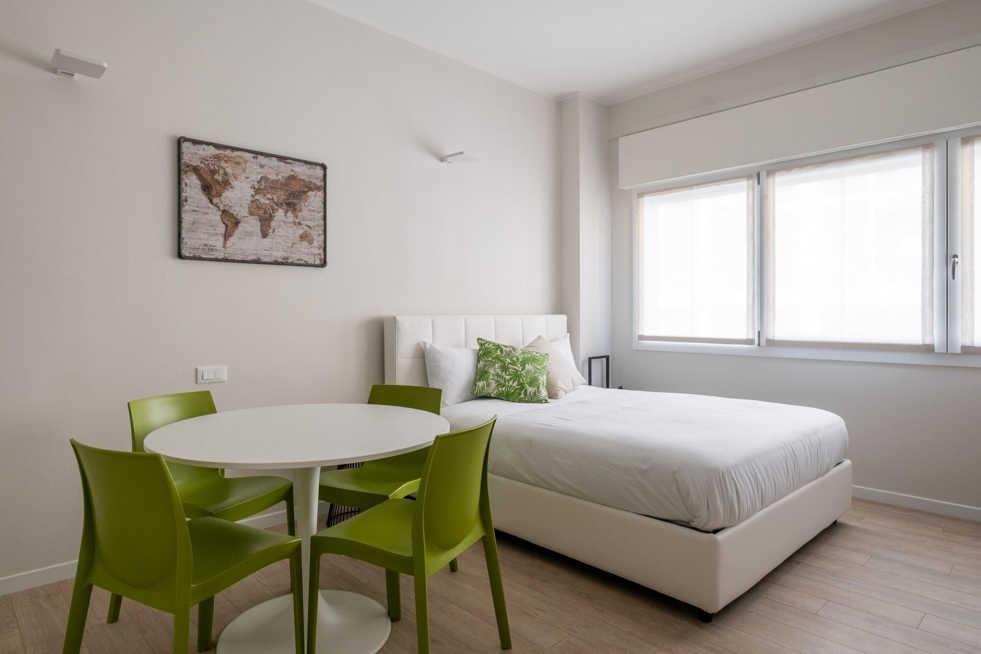 Un dormitorio con una cama, una mesa redonda y cuatro sillas verdes.