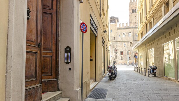 A narrow cobblestone street with historic buildings, a closed wooden door, a no parking sign, and a motorcycle parked on the side.