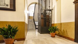 A hallway with a tiled floor, two potted plants, a staircase, and a metal elevator.