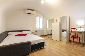 A bedroom with a bed, a desk, a chair, and a mirror.