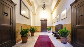 A hallway with a red carpet, wooden doors, potted plants, a bench, and framed pictures on the walls.