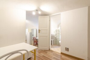 A hallway with a white door leading to a bathroom. There is a white table with a yellow frame and a white chair in the foreground.