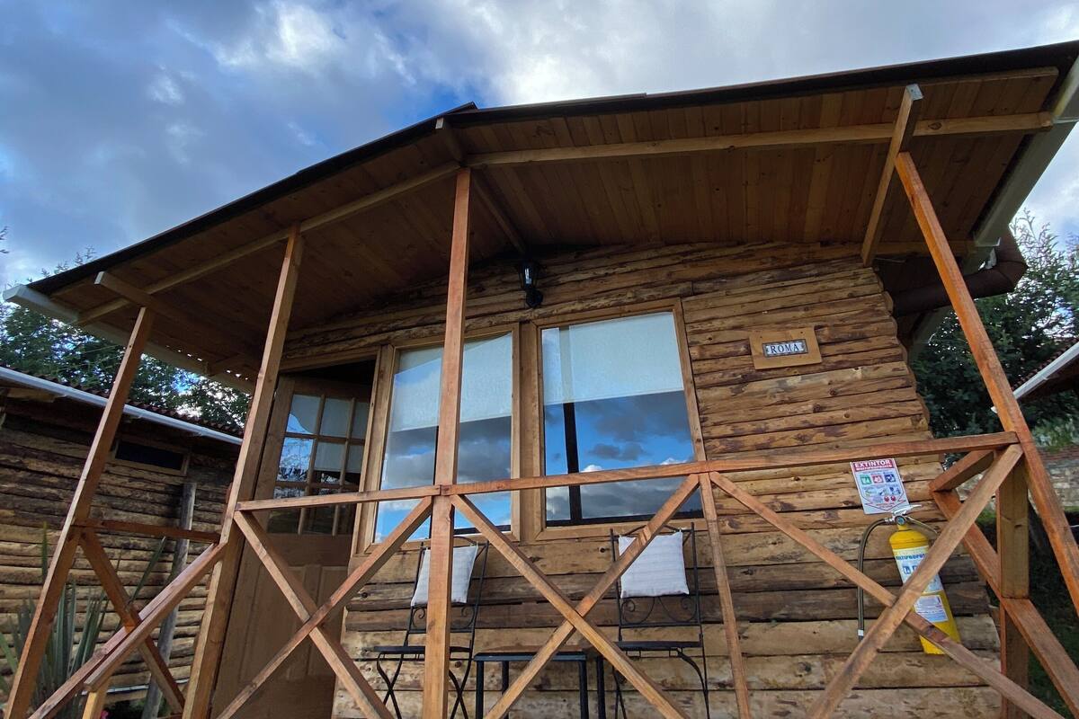 A wooden cabin with a covered porch, multiple windows, and a sign indicating "ROMA".