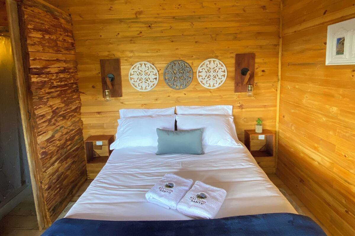 A wooden cabin room with a bed, two wall-mounted decorative plates, and a nightstand with a glass.