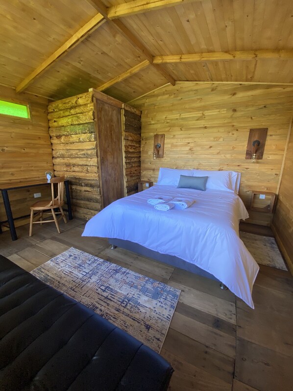 A wooden cabin bedroom with a bed, a chair, and a small table. - Cabañas el refugio del santo (Guasca)