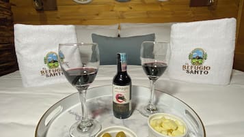 Una mesa de comedor con una botella de vino, dos copas, un cuenco de aceitunas y un cuenco de queso.