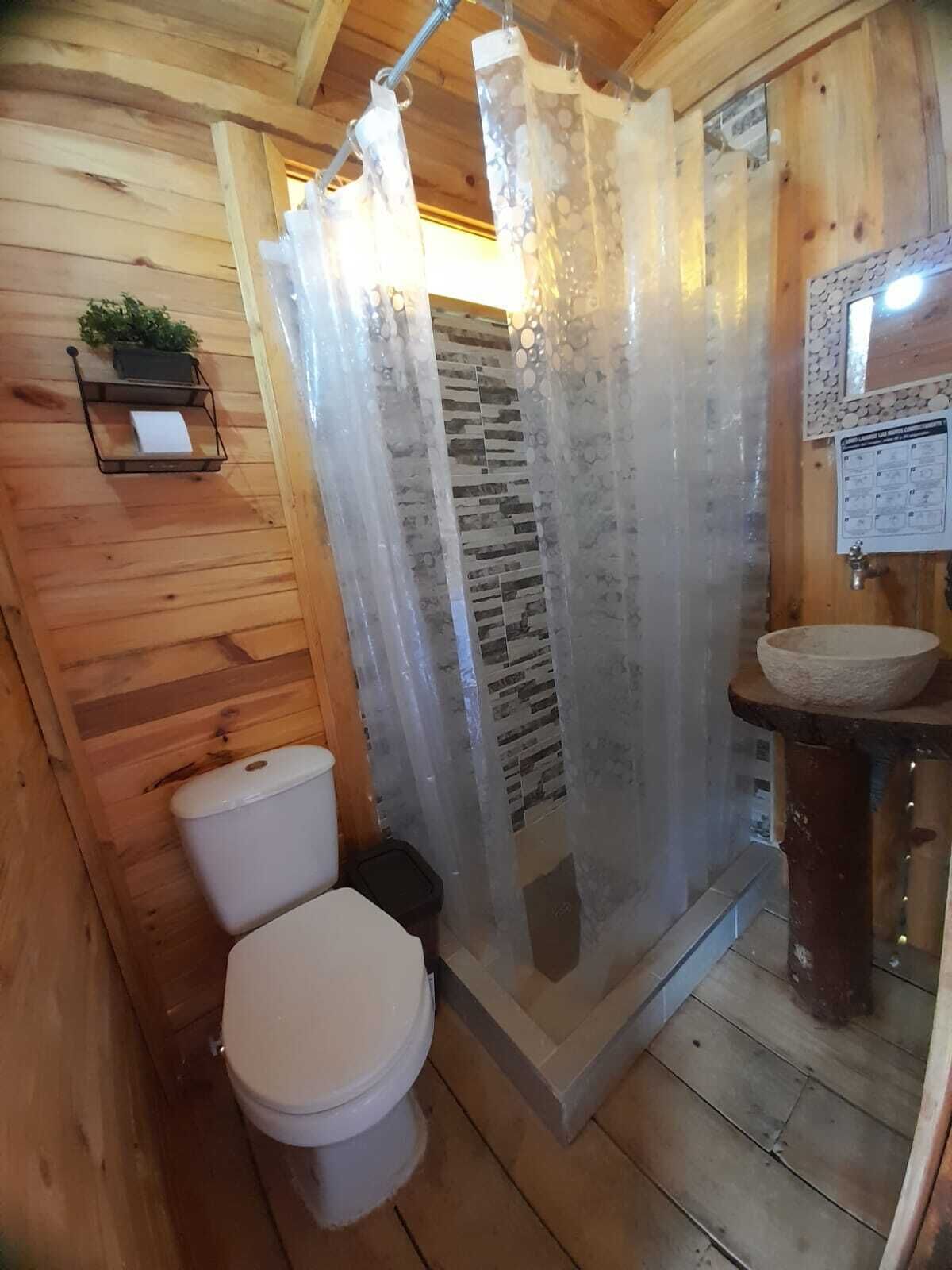 A wooden cabin bathroom with a toilet, shower curtain, and a stone sink.