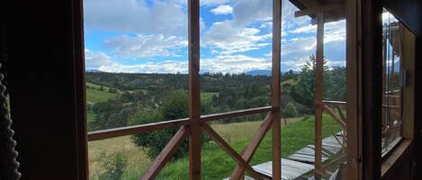 A view from a window with a wooden frame and a view of a green landscape with hills and a blue sky.