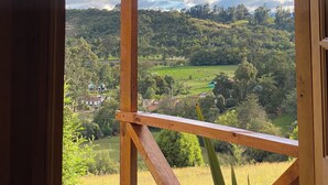 Un balcon en bois offrant une vue sur un paysage verdoyant et des maisons situées au loin.