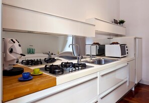 A modern kitchen with a gas stove, sink, and white cabinetry. - Elegant Apartment at Chiaia by Wonderful Italy (Naples)