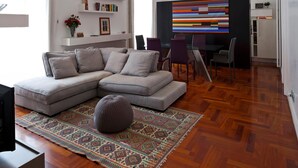 A modern living room with a sectional sofa, a glass dining table with chairs, a colorful abstract painting, and a patterned rug. - Elegant Apartment at Chiaia by Wonderful Italy (Naples)