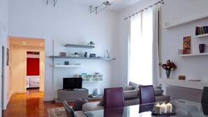 A modern living room with a glass dining table, comfortable seating, a flat-screen TV, and decorative shelves. - Elegant Apartment at Chiaia by Wonderful Italy (Naples)