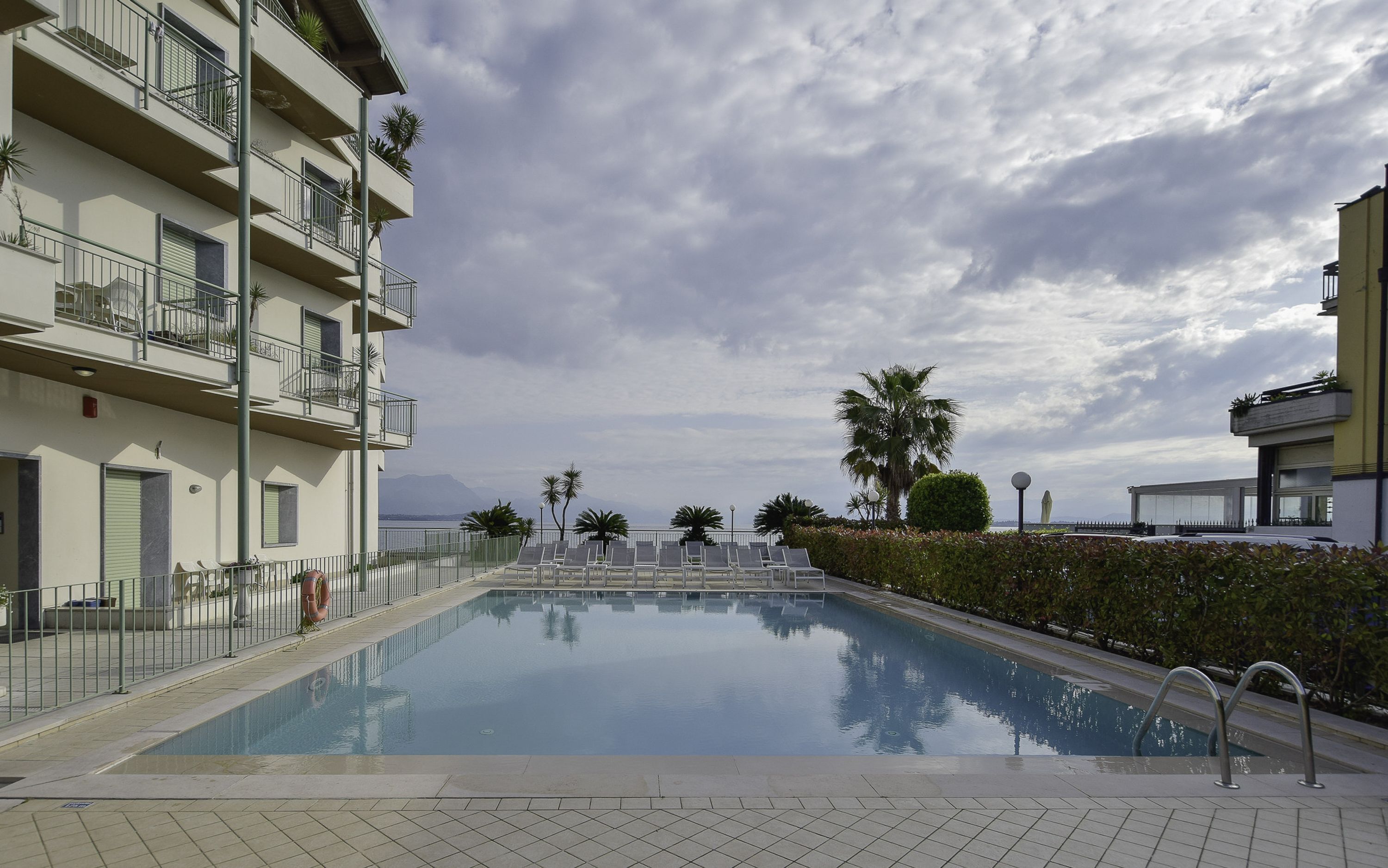 A swimming pool with a tiled deck, surrounded by a low fence and palm trees.