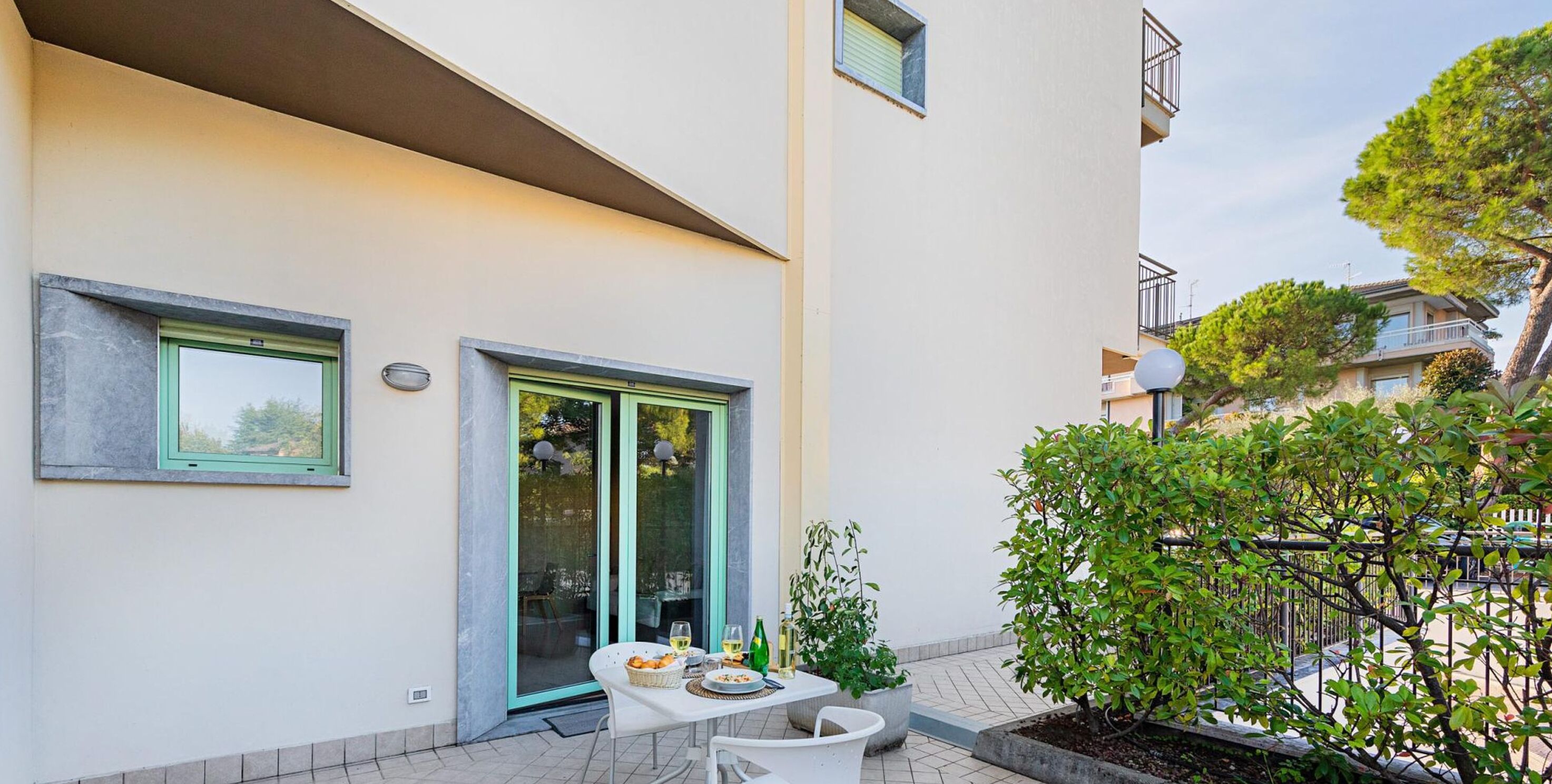A modern apartment with a balcony, a dining area with outdoor seating, and a view of neighboring buildings.