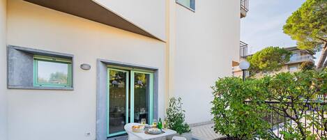 A modern apartment with a balcony, a dining area with outdoor seating, and a view of neighboring buildings.