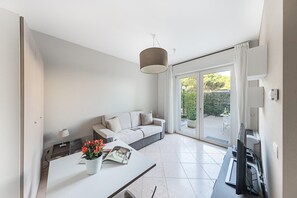 A modern living room with a sofa, a coffee table with flowers, a lamp, and a TV. - Residenza Miralago With Pool - Ground Floor Studio Apartment (Desenzano del Garda)