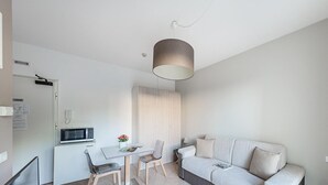 A modern, minimalist room with a sofa, a dining table, and a microwave. - Residenza Miralago With Pool - Ground Floor Studio Apartment (Desenzano del Garda)